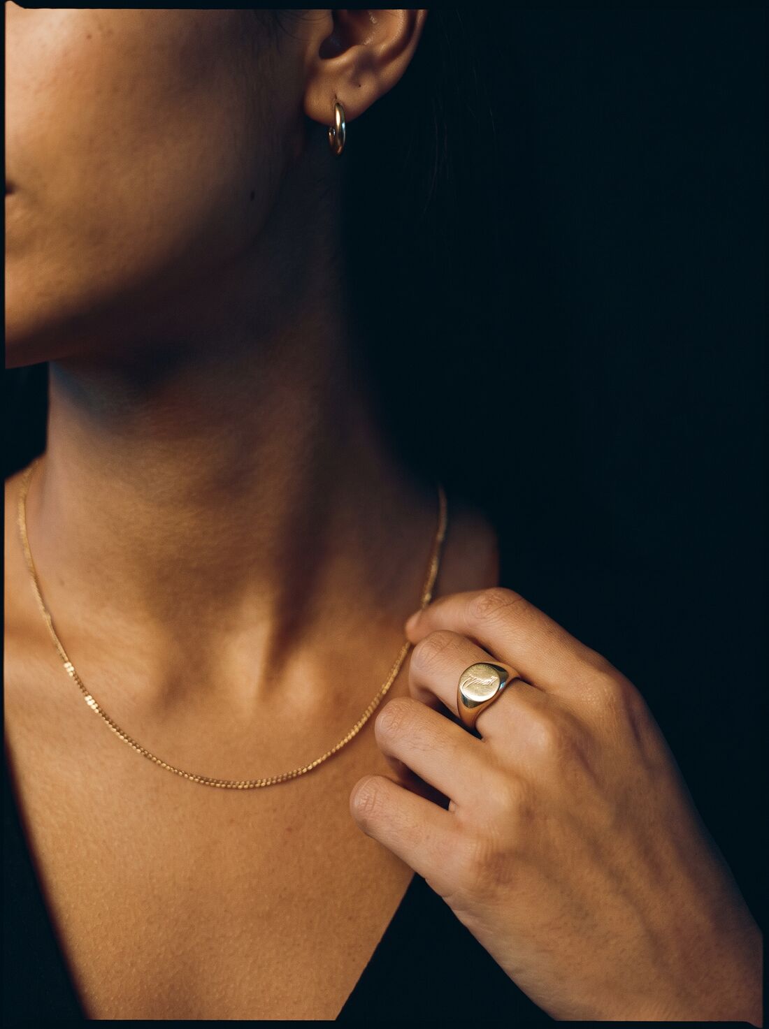 Fine gold chain, signet ring and hoop earrings on warm skin