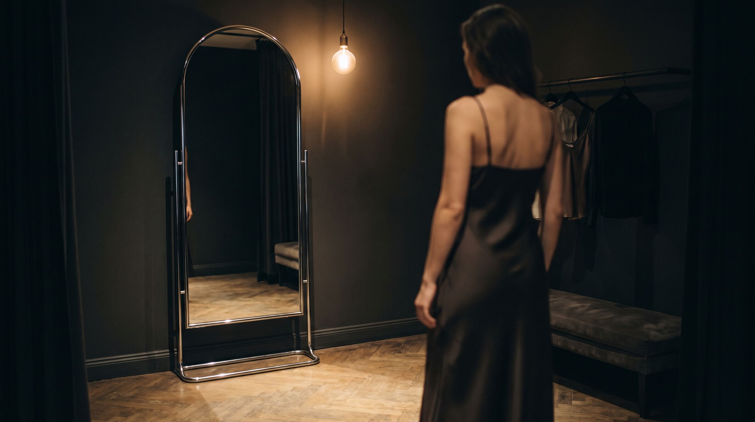 A chrome-framed mirror in a dim fitting room, lit by a single warm bulb